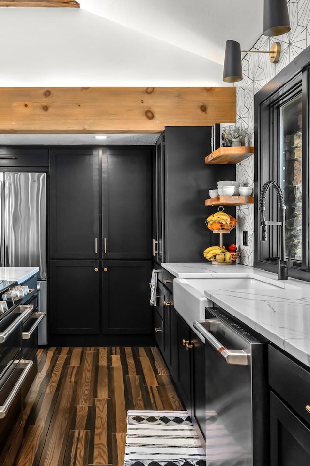 kitchen with light stone counters, open shelves, dark cabinetry, dark wood finished floors, and stainless steel appliances