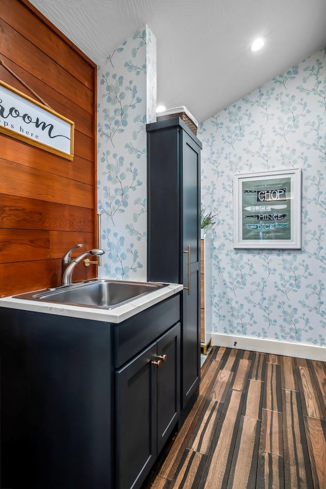 kitchen featuring baseboards, wallpapered walls, dark wood-style flooring, a sink, and vaulted ceiling