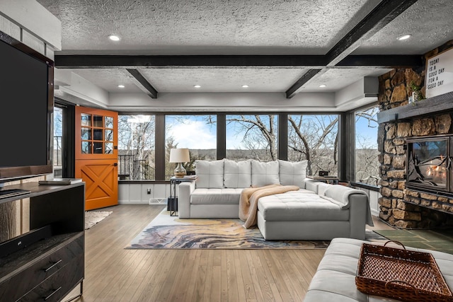 living room featuring beamed ceiling, a textured ceiling, a stone fireplace, and hardwood / wood-style floors