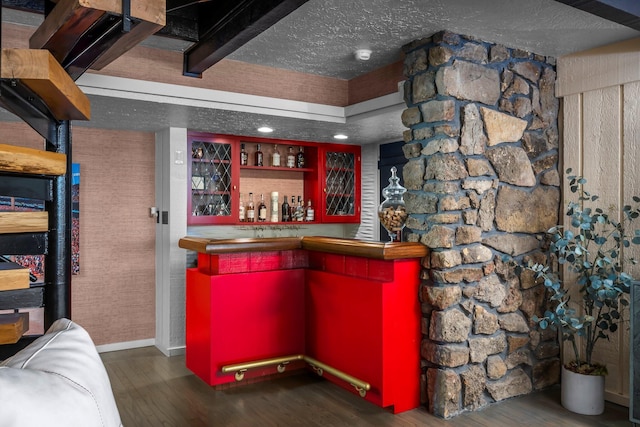 bar with a textured ceiling, a bar, baseboards, and wood finished floors