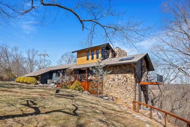 view of front of home with a front yard, stone siding, and a shingled roof