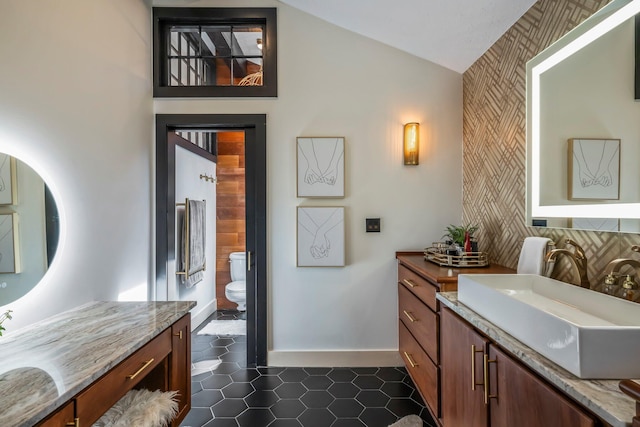 bathroom featuring toilet, lofted ceiling, wallpapered walls, baseboards, and vanity