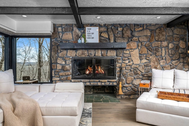 living area featuring beamed ceiling, a textured ceiling, a stone fireplace, and wood finished floors