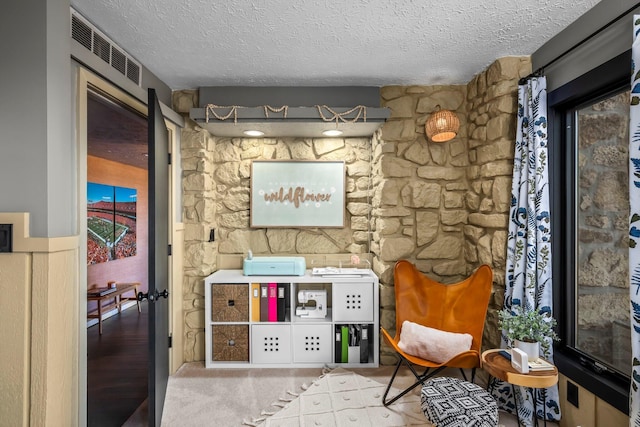 sitting room with carpet, visible vents, and a textured ceiling