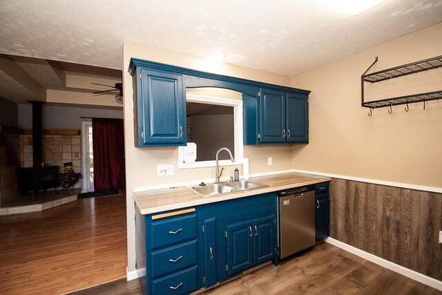 kitchen featuring dishwasher, a wood stove, blue cabinets, and a sink