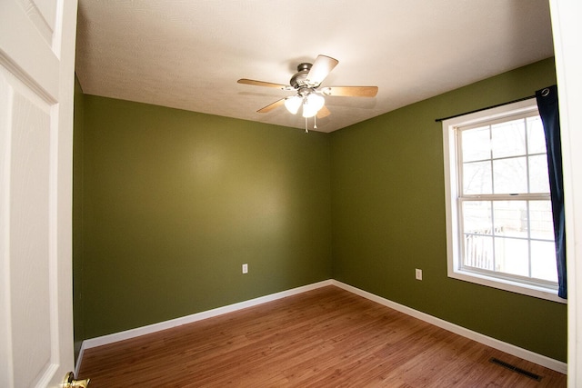 empty room featuring visible vents, ceiling fan, baseboards, and wood finished floors