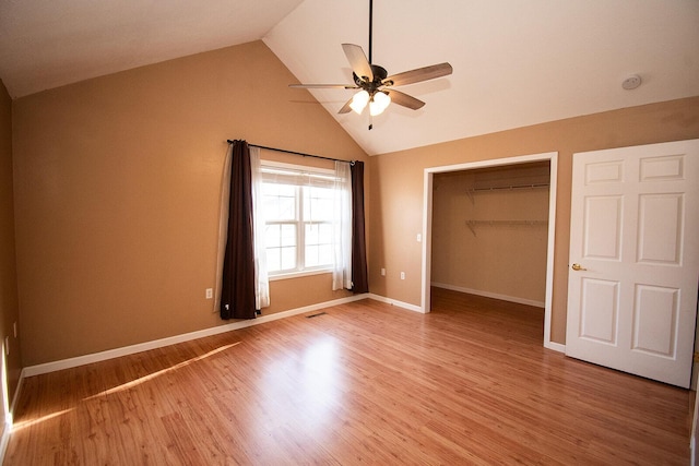 unfurnished bedroom featuring a spacious closet, baseboards, lofted ceiling, light wood-style flooring, and a closet