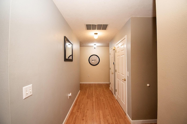 corridor featuring visible vents, light wood-type flooring, and baseboards