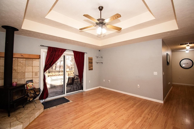 spare room featuring a tray ceiling, visible vents, wood finished floors, and a wood stove