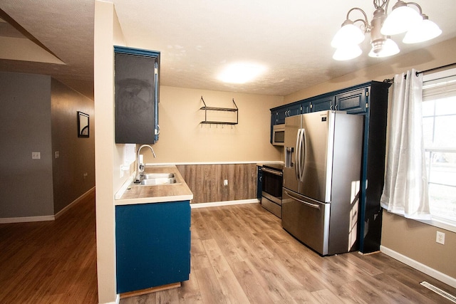 kitchen with a chandelier, light countertops, stainless steel appliances, blue cabinets, and a sink