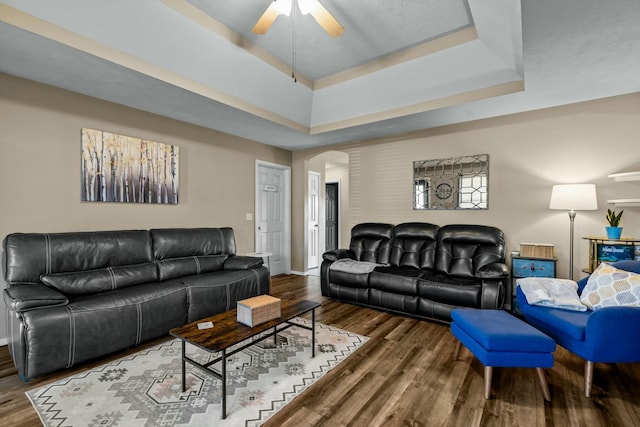 living area featuring a raised ceiling, a ceiling fan, wood finished floors, arched walkways, and baseboards