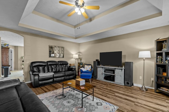 living area featuring baseboards, ceiling fan, wood finished floors, arched walkways, and a raised ceiling