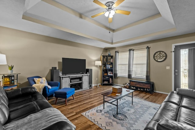 living room with a raised ceiling, wood finished floors, and ceiling fan