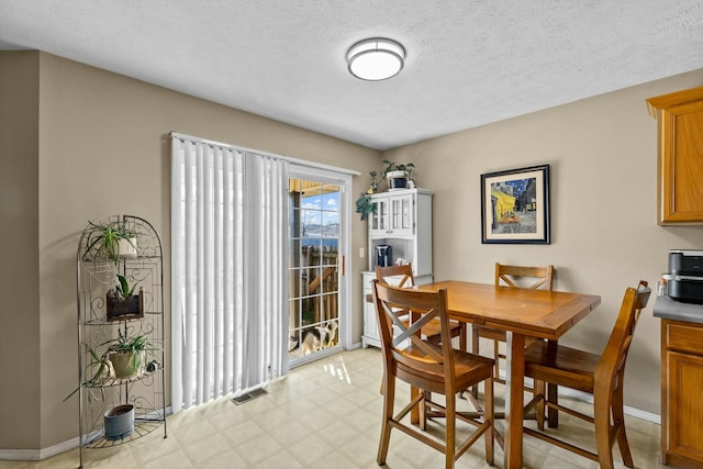 dining space featuring visible vents, light floors, a textured ceiling, and baseboards