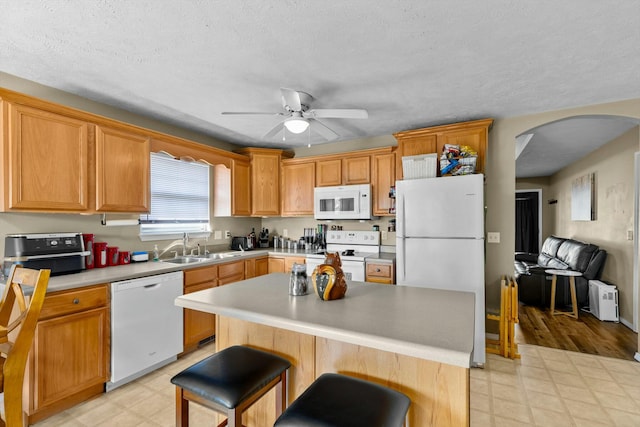 kitchen with white appliances, light floors, arched walkways, a sink, and ceiling fan