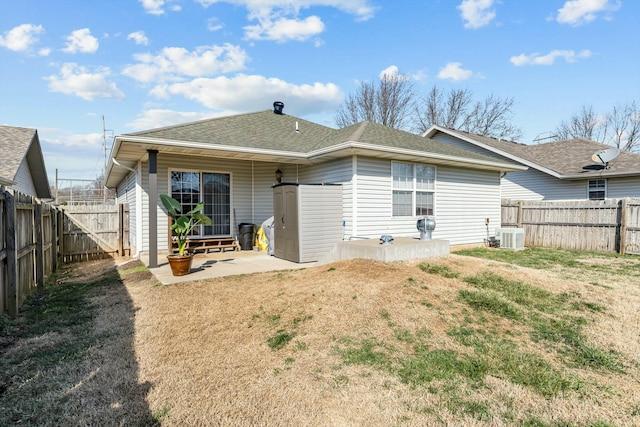 back of house with a fenced backyard, a lawn, a shingled roof, and a patio