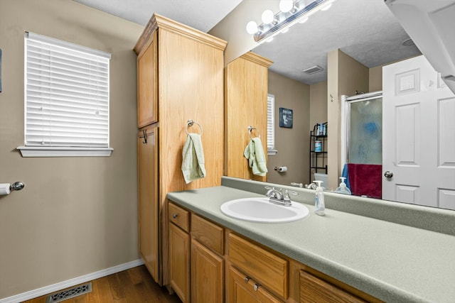 full bath with visible vents, a stall shower, wood finished floors, baseboards, and vanity