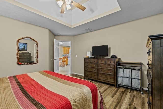 bedroom featuring visible vents, a raised ceiling, baseboards, and wood finished floors