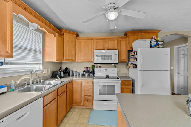 kitchen with a ceiling fan, a sink, white appliances, arched walkways, and light countertops