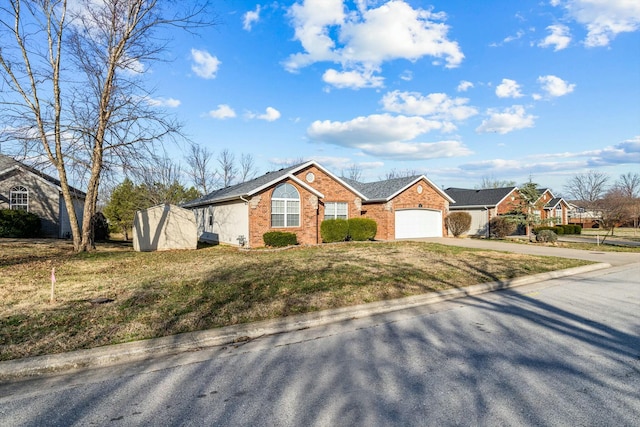 view of front of house featuring driveway, a storage shed, an attached garage, a front yard, and brick siding