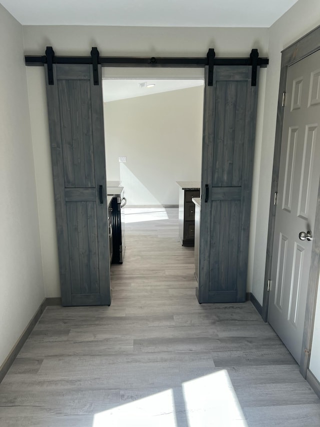 hall with light wood-type flooring, a barn door, and baseboards