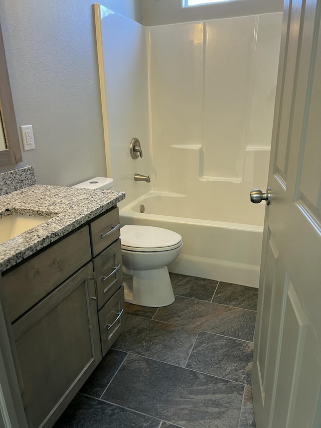 full bathroom featuring toilet, stone tile floors, bathtub / shower combination, and vanity