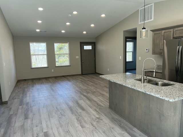 kitchen with visible vents, light wood-type flooring, a sink, light stone counters, and vaulted ceiling