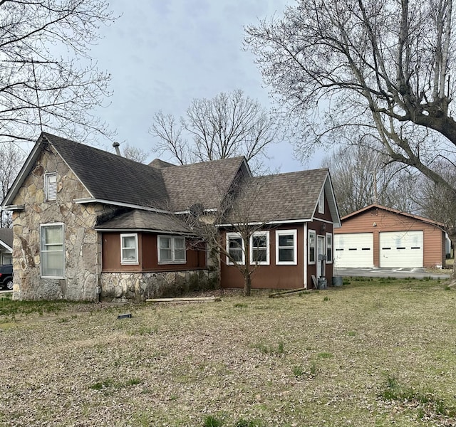 view of front of property featuring an outdoor structure, a front yard, stone siding, and roof with shingles