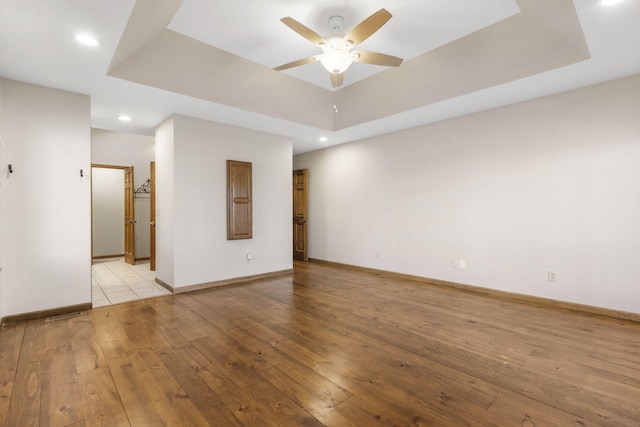 empty room with a ceiling fan, a raised ceiling, light wood-style floors, and baseboards