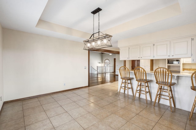 kitchen featuring a breakfast bar area, a tray ceiling, built in microwave, light countertops, and white cabinets