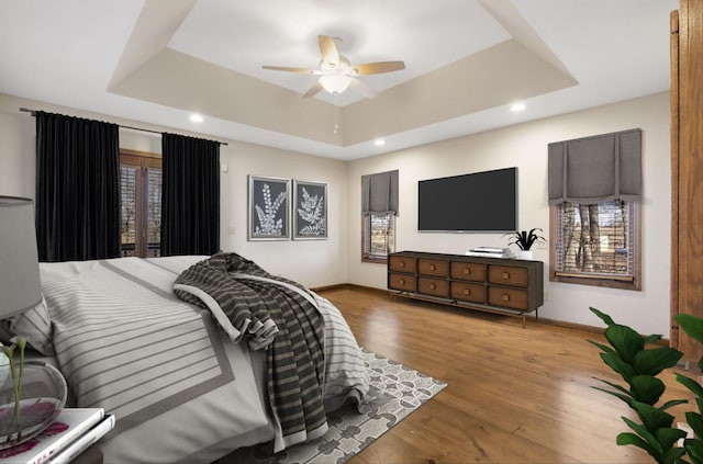 bedroom featuring recessed lighting, baseboards, a tray ceiling, and wood-type flooring