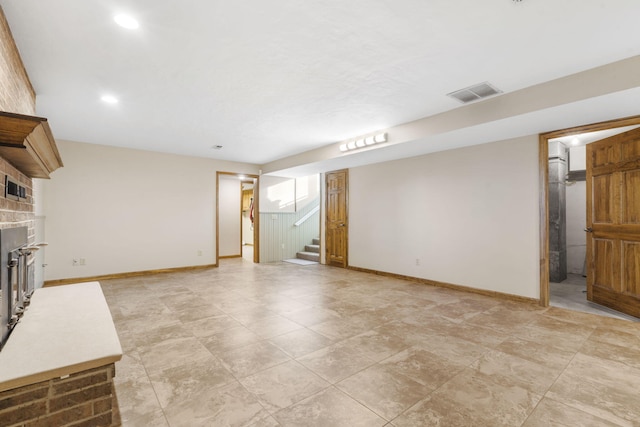 unfurnished living room with visible vents, baseboards, a brick fireplace, and stairs