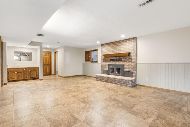 unfurnished living room featuring visible vents, a brick fireplace, a sink, and a wainscoted wall