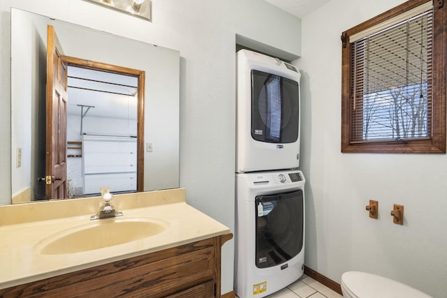 bathroom featuring toilet, vanity, baseboards, and stacked washer and dryer