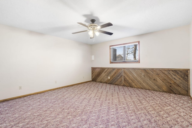 unfurnished room featuring wood walls, baseboards, a ceiling fan, and carpet floors