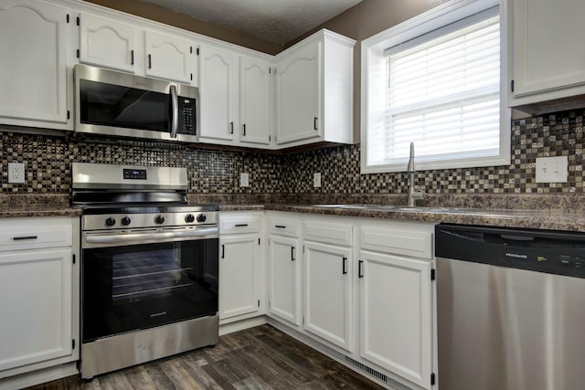 kitchen with dark countertops, appliances with stainless steel finishes, white cabinetry, and dark wood-type flooring