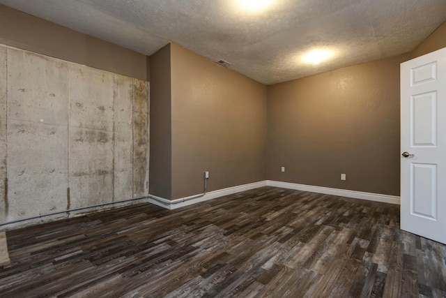 empty room with dark wood finished floors, a textured ceiling, and baseboards