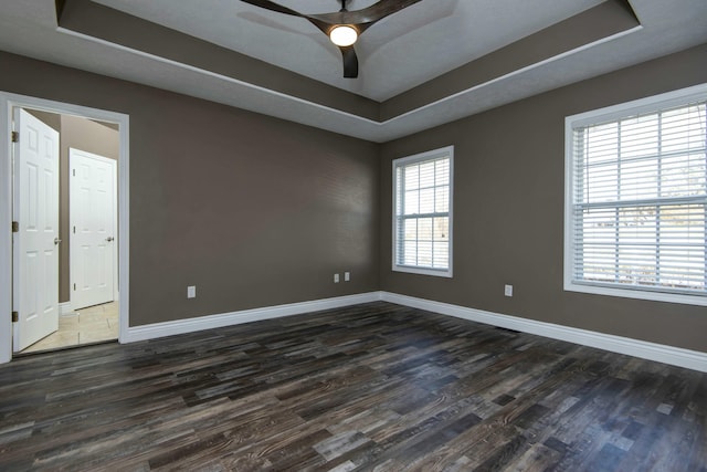 unfurnished room with dark wood finished floors, baseboards, and a tray ceiling