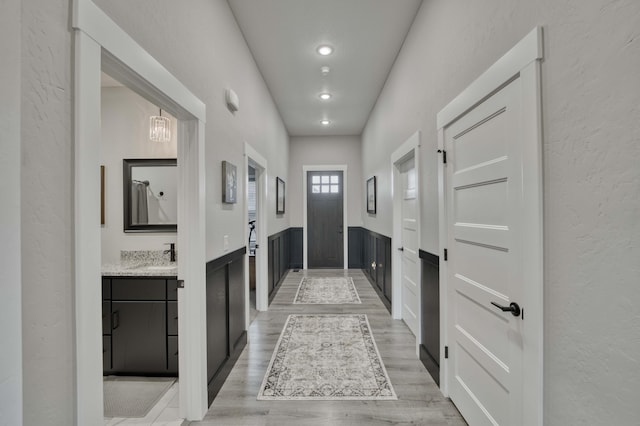 interior space with a wainscoted wall, light wood-style flooring, a textured wall, and a sink