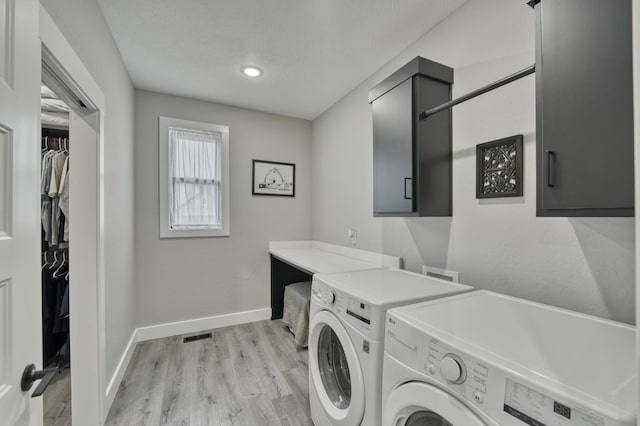 clothes washing area with baseboards, separate washer and dryer, cabinet space, light wood-style floors, and a textured ceiling