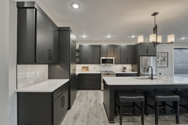 kitchen featuring a breakfast bar, a sink, light countertops, appliances with stainless steel finishes, and decorative light fixtures