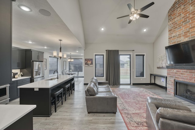 living area featuring high vaulted ceiling, recessed lighting, a brick fireplace, ceiling fan with notable chandelier, and light wood-type flooring