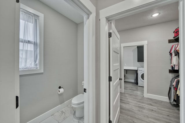 bathroom with baseboards, toilet, marble finish floor, and washer / clothes dryer