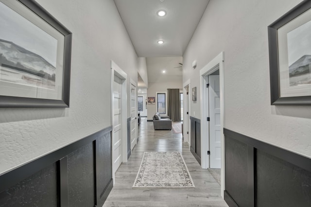 hallway with recessed lighting, light wood-style flooring, wainscoting, and a textured wall