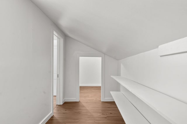 hallway with baseboards, lofted ceiling, and wood finished floors