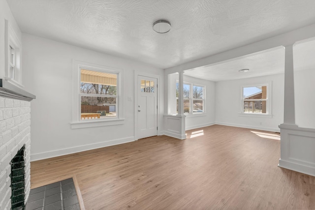 unfurnished living room with baseboards, light wood-type flooring, a fireplace, a textured ceiling, and ornate columns