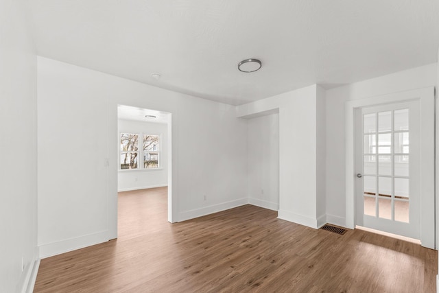 unfurnished room with wood finished floors, visible vents, and baseboards