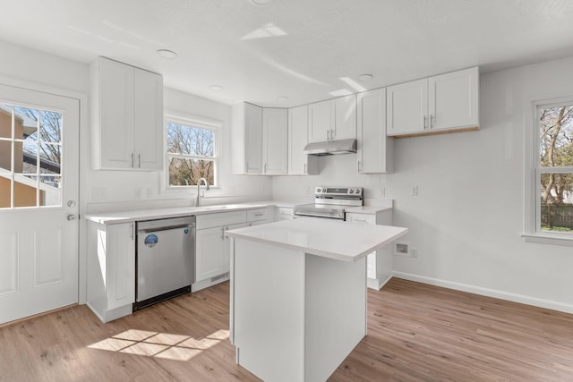 kitchen with light wood-style flooring, stainless steel appliances, light countertops, white cabinets, and under cabinet range hood