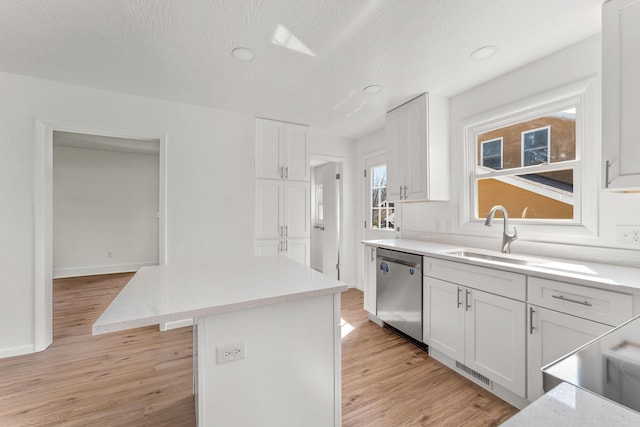 kitchen with a center island, light wood-type flooring, stainless steel dishwasher, white cabinetry, and a sink