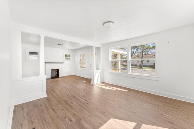 unfurnished living room with baseboards, light wood-style floors, a healthy amount of sunlight, and a fireplace